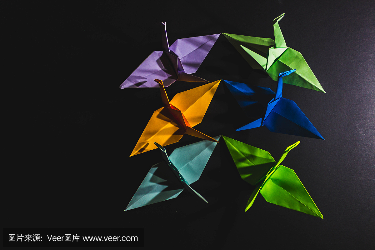 纸鹤折纸由不同颜色的纸组成。纸鹤是用折纸技术在黑暗的背景上制作的。纸鹤,排在右边。